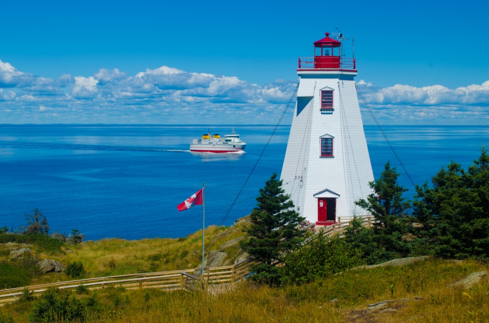 A lighthouse on the coast of New Brunswick, Canada with a sailing boat heading across the horizon.